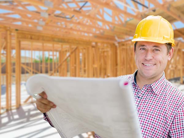 Male contractor standing in a new home build with blueprints in his hand.